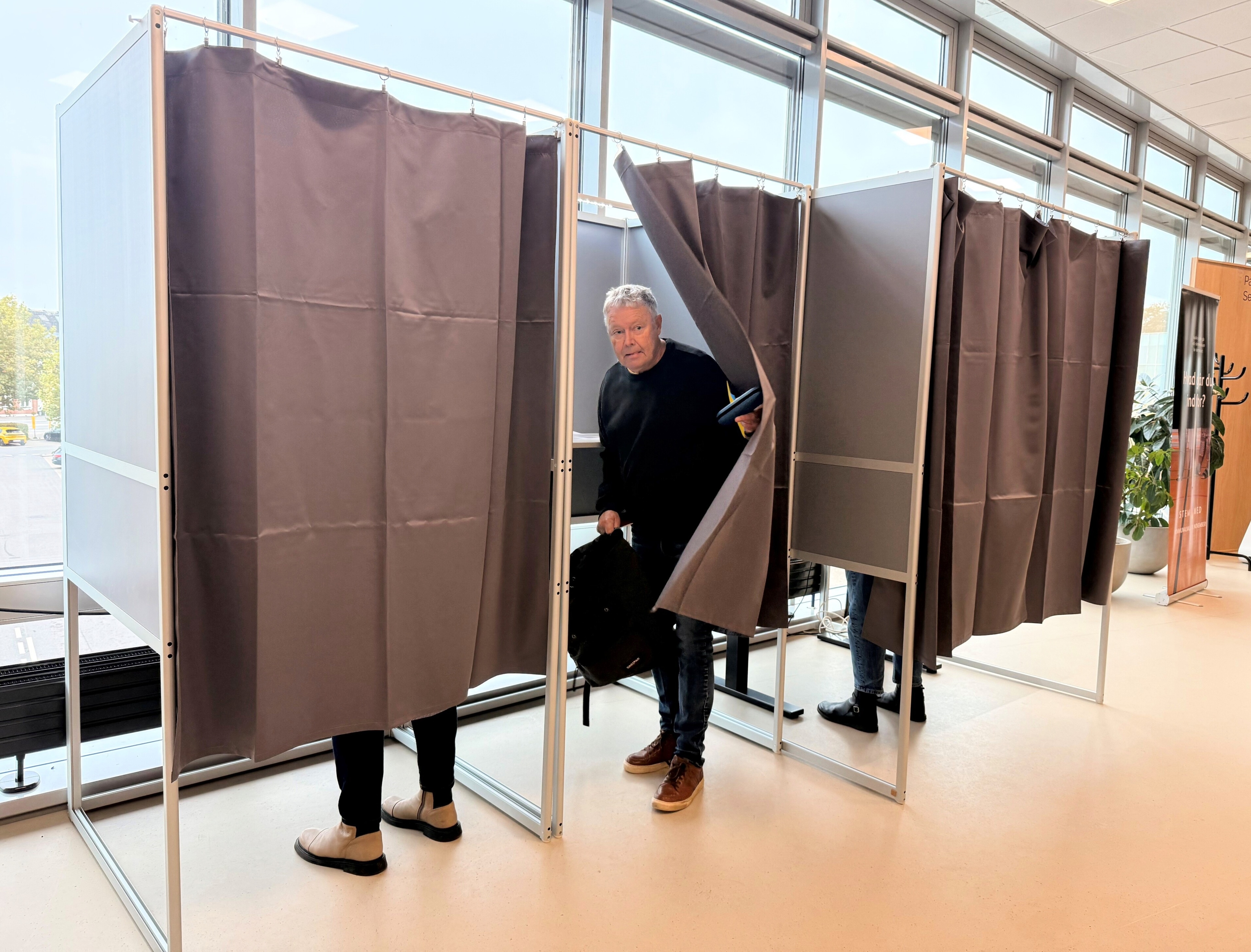 Foto af tre stemmebokse i Borgerservice, hvor mand træder ud bag gardinet efter at have sat sit kryds.
